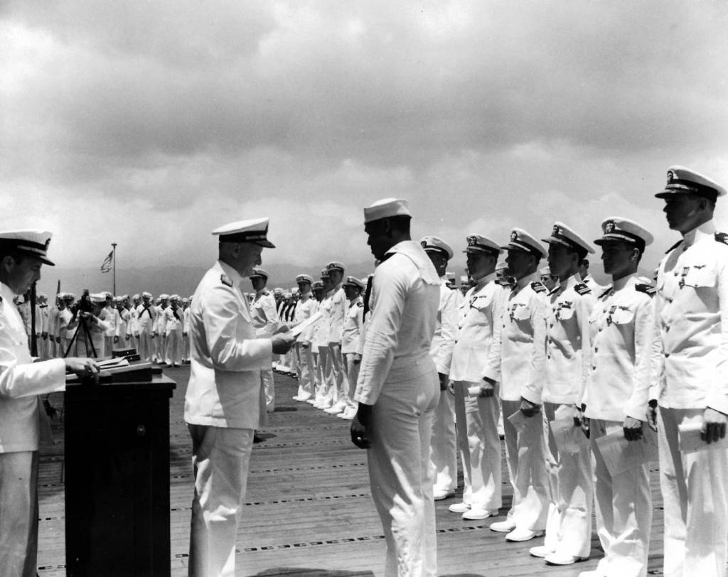 Mess Attendant 2nd Class Doris Miller receives the Navy Cross from Adm. Chester W. Nimitz at a ceremony held on the flight deck of the aircraft carrier Enterprise at Pearl Harbor, 27 May 1942. 