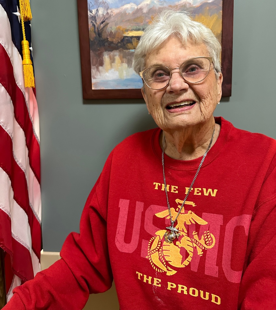Smiling woman wearing U.S. Marine Corps sweatshirt standing next to an American flag.